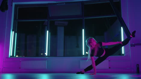 una mujer hace yoga y se estira en una hamaca colgante a la luz del neón. una chica joven y delgada practicando yoga con mosca en el gimnasio.