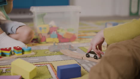 camera focuses on the hands of two children playing with cars and pieces of wood sitting on a carpet in a montessori school