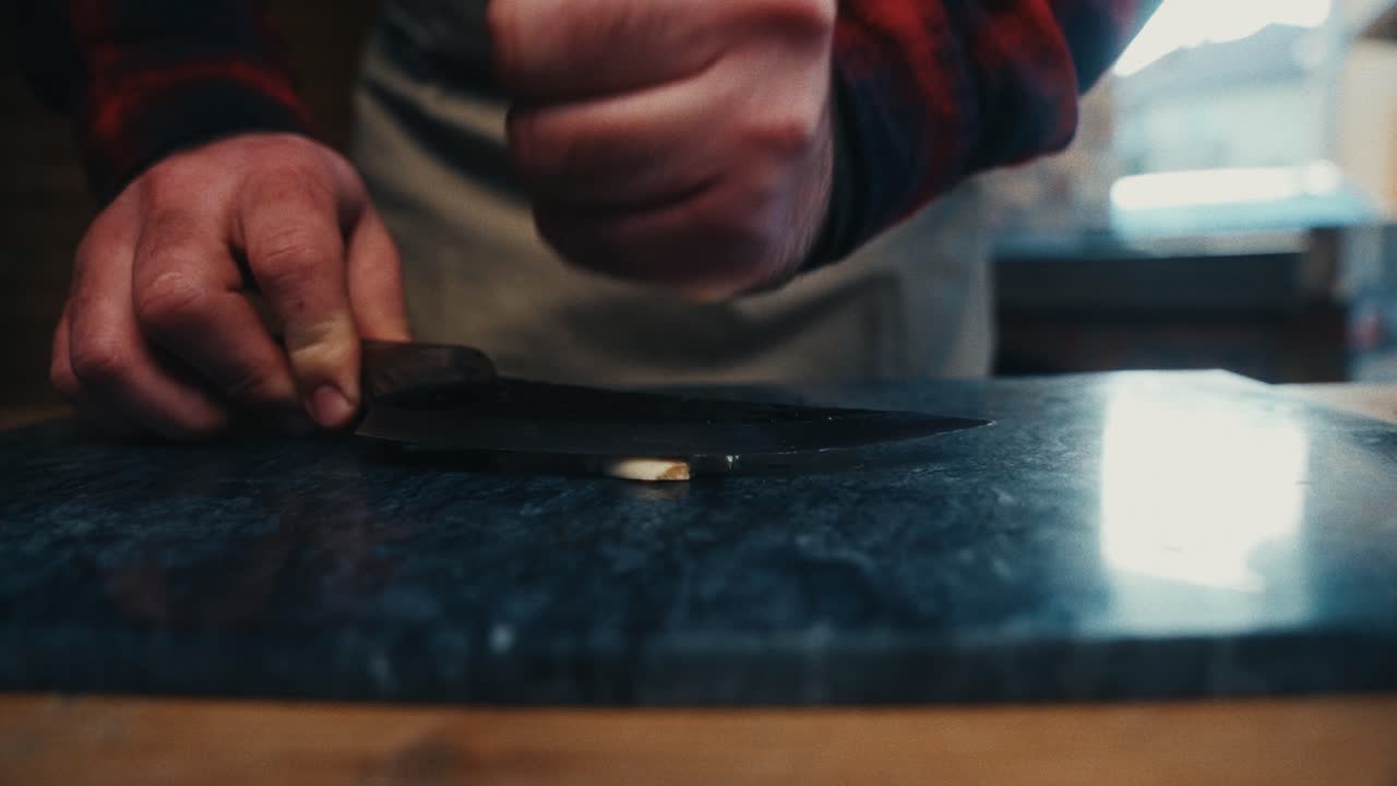A close-up of a chef slicing seafood with a knife on a stone surface indoors