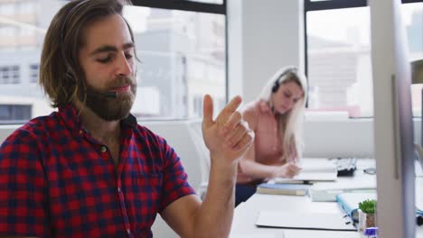 hombres de negocios caucásicos que usan auriculares hablando con clientes en una oficina moderna