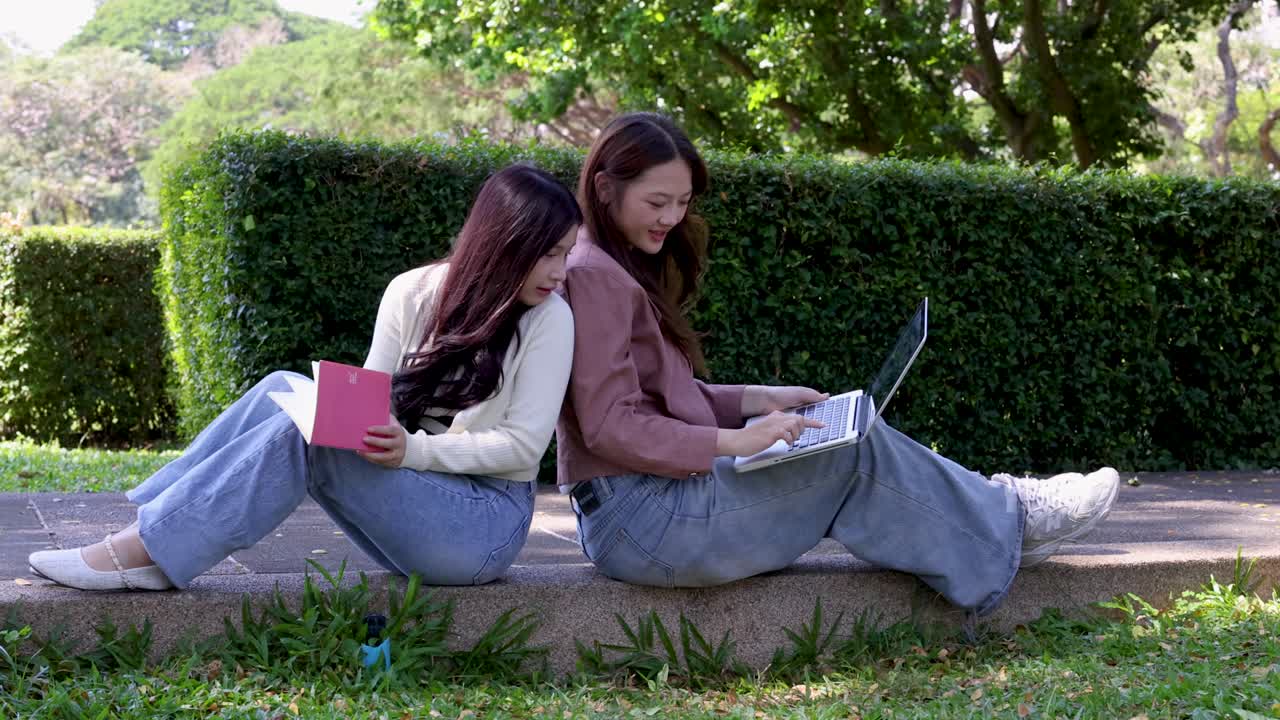 屋外の石の台に背中合わせに座り、ノートパソコンとノートを使用する二人の学生。