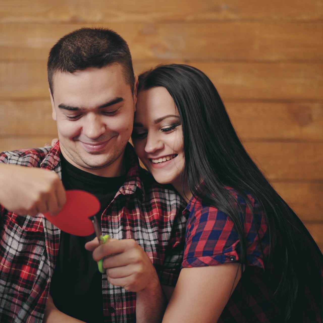 Um homem está recortando um coração com papel colorido nos braços de uma mulher amada no Dia dos Namorados.