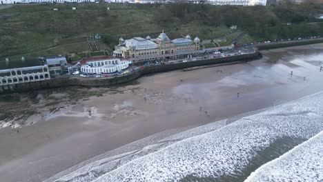 Filmische-Aufnahme-Der-Kontinuierlichen-Gezeiten-Am-Strand-Mit-Einigen-Leuten,-Die-Neben-Dem-Scarborough-Spa-Im-Norden-Von-Yorkshire,-England,-Spaß-Haben