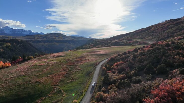 Luce che si riflette su un Airstream argentato mentre sfreccia lungo una vecchia strada di campagna durante il pieno foliage autunnale in Colorado.