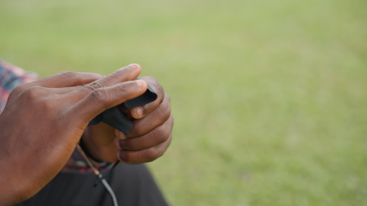 Closeup black father handing sunglasses to son on grassy bench, folded case and chain tucked inside, small gift exchange layered with memory and warmth, gentle offer and grateful receive, quiet family