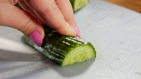 female slicing fresh cucumber in half on plastic board, close up view