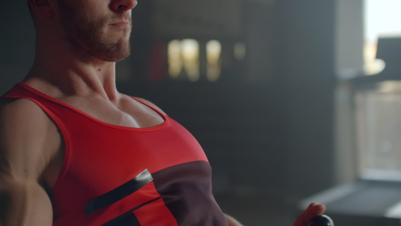 체육 클럽에서 전력 운동 기계와 함께 등에서 운동하는 운동을 하는 운동적인 셔츠 없는 남성. 체육관에서 로잉 기계를 사용하는 근육적인 남자의 측면 시각