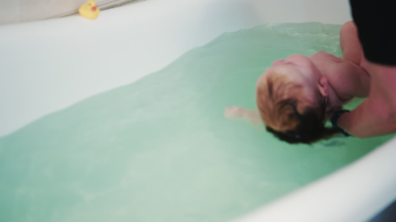 Bebè sdraiato in una vasca da bagno che si gode il bagnetto con il supporto di un adulto.