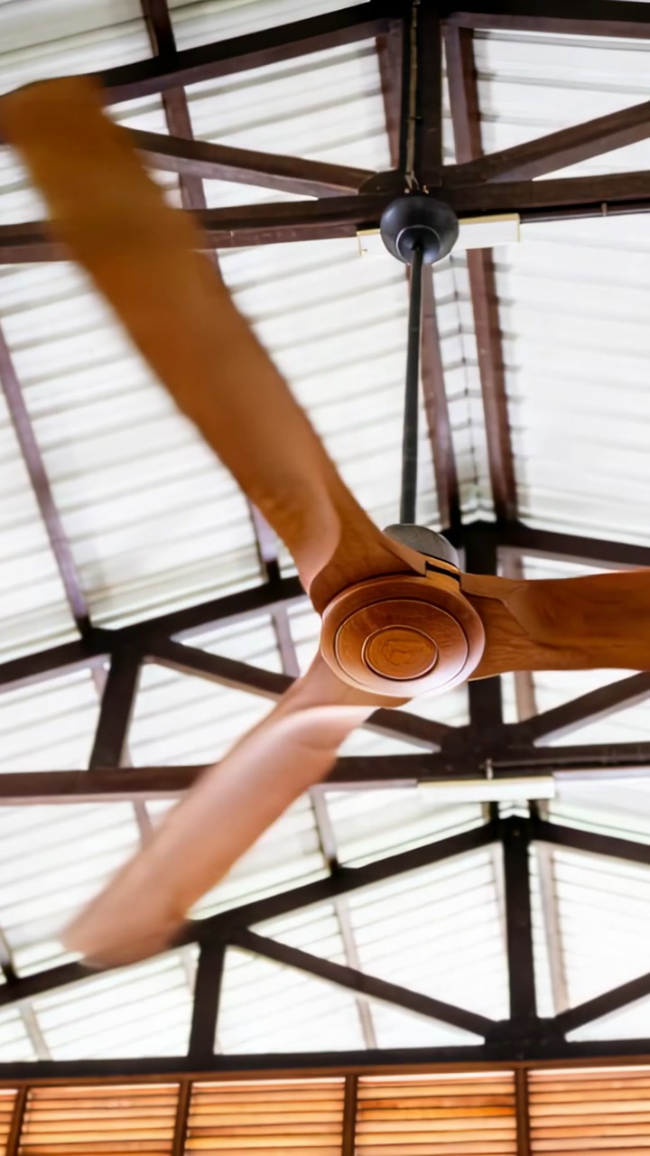 Vertical video: Spinning ceiling fan drawing power under corrugated roof, creating blade blur