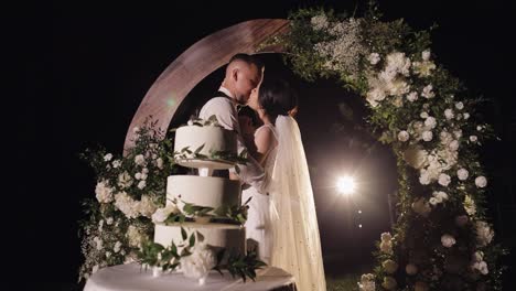 newlyweds making a kiss near cake, lovely bride and groom couple with three-tiered wedding dessert