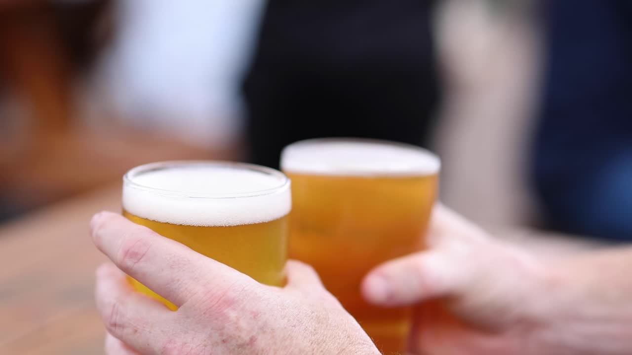 Close-up of hands holding frothy beer glasses over a wooden table, capturing a moment of shared enjoyment.