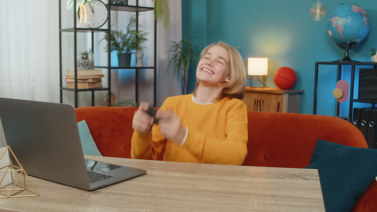 Teenager boy playing sports simulator game on laptop with joystick celebrating goal victory at home