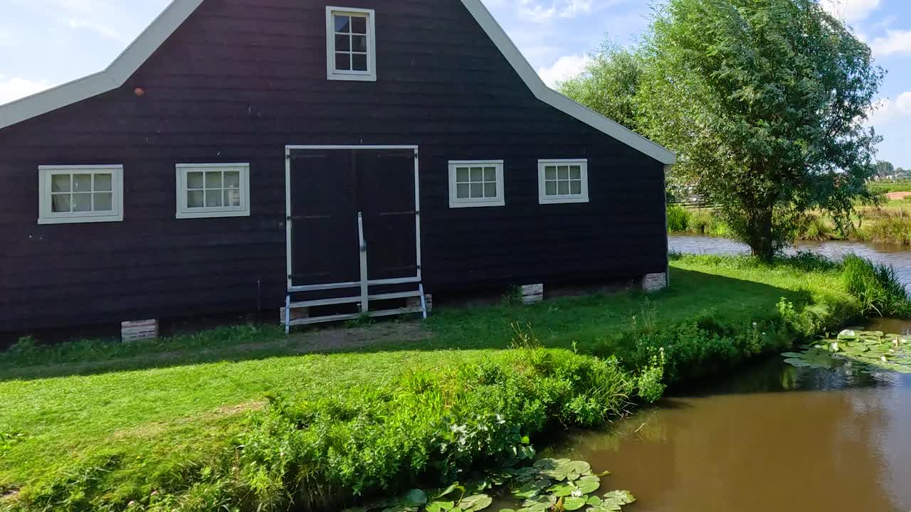 Smooth daytime pan reveals rural Dutch house, windmills, canal, green fields, and blue sky