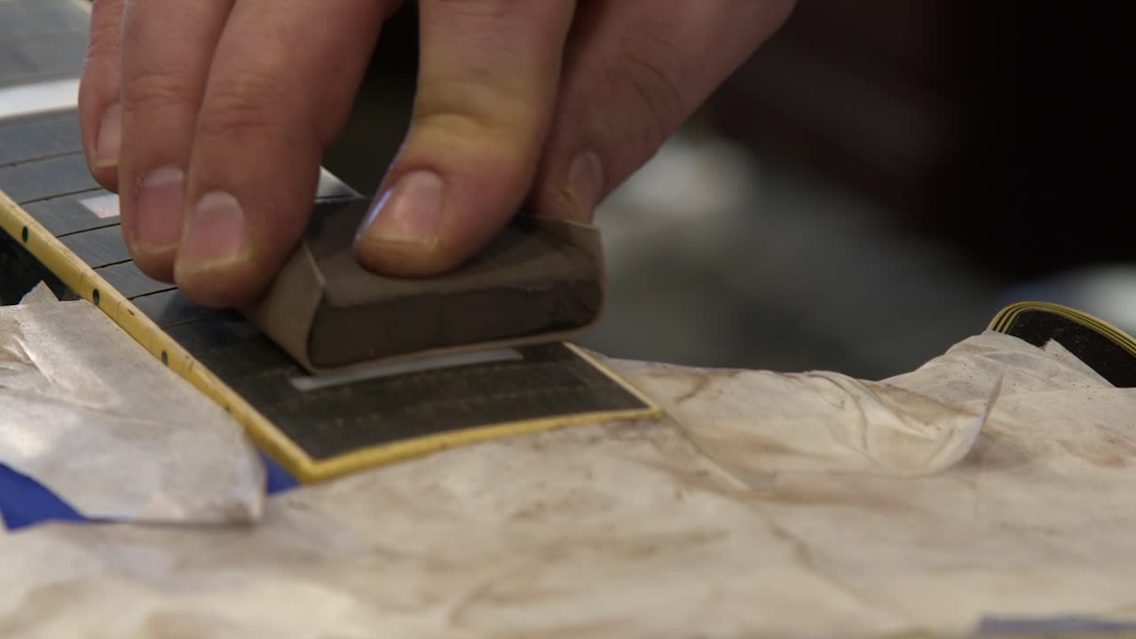 Closeup technician hands sanding ebony guitar fretboard for repair