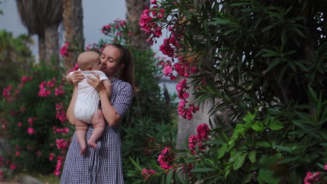 Amid-palm-trees-and-blooming-flowers-at-the-resort,-a-mother-joyfully-plays,-hugs,-and-showers-kisses-on-her-child.-This-scene-embodies-a-happy-family-moment