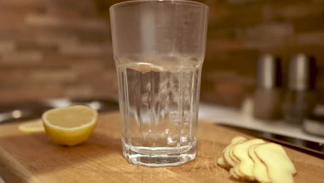 Pouring-hot-water-from-the-kettle-into-the-glass-standing-next-to-sliced-ginger-and-lemon,-STILL,-4k