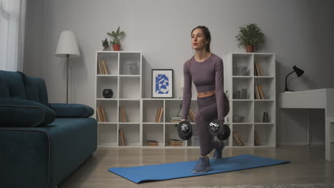 athletic woman is training in living room at weekends squatting with dumbbells in hands working muscles of legs and buttocks wellness and fitness concept