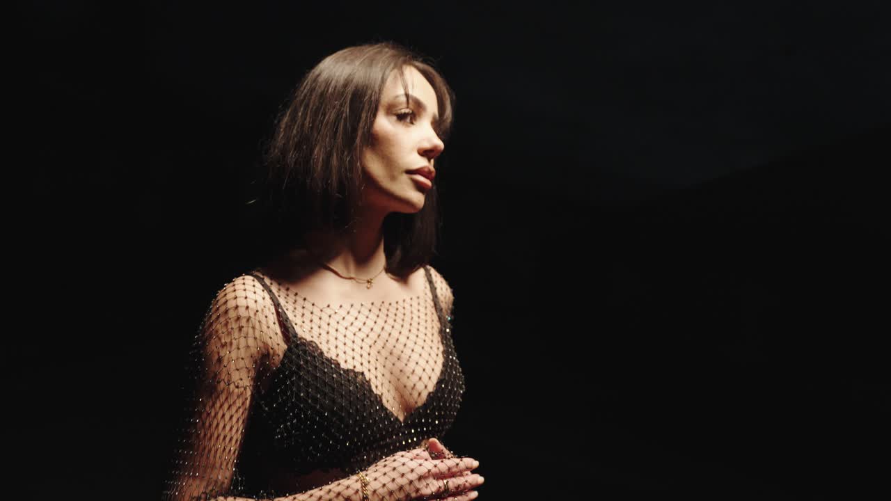 lightly dressed beautiful young woman in a dark environment posing from the side close up