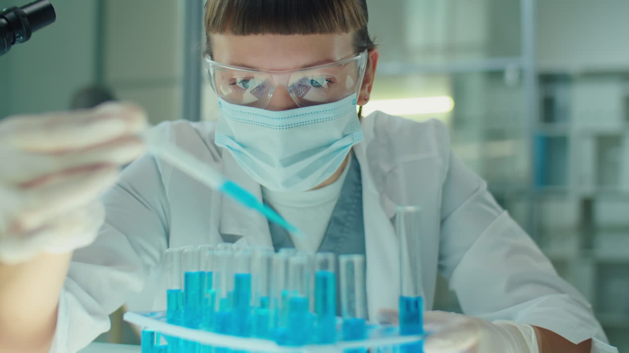 Female Microbiologist in Mask and Gloves Working with Blue Liquid in Lab