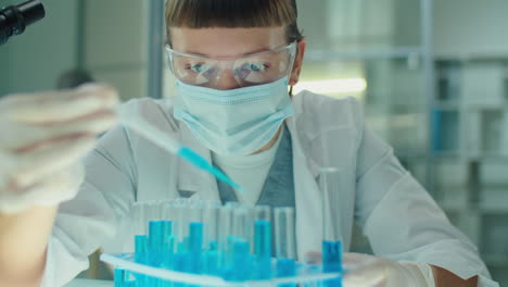 female microbiologist in mask and gloves working with blue liquid in lab