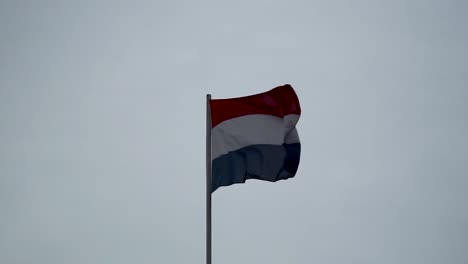 dutch flag waving against cloudy, grey sky