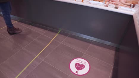 los letreros de calcomanías de distanciamiento social en un piso de delicatessen indican dónde debe pararse un cliente
