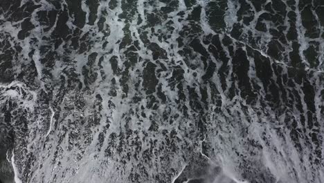 top view of pererenan beach in bali indonesia with waves crashing on the dark volcanic sand, aerial looking down shot