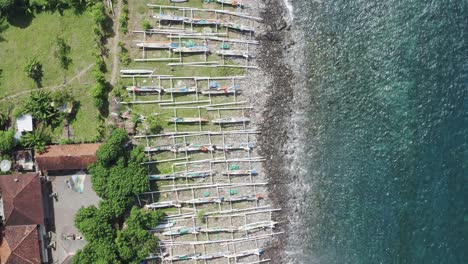 amed beach in bali indonesia with jukung fishing boats lined up on the shore, aerial top view pan down shot