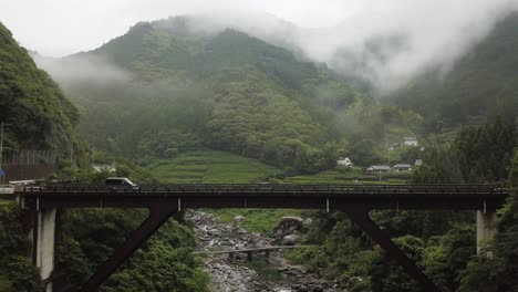 Van-driving-over-a-picturesqe-bridge-with-foggy-mountains-and-a-river-below