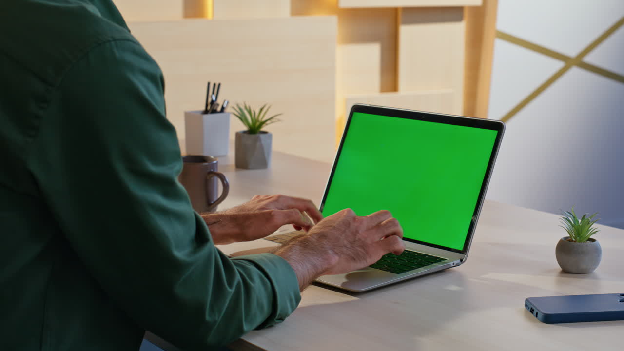 Man Typing on Laptop with Green Screen in Workspace