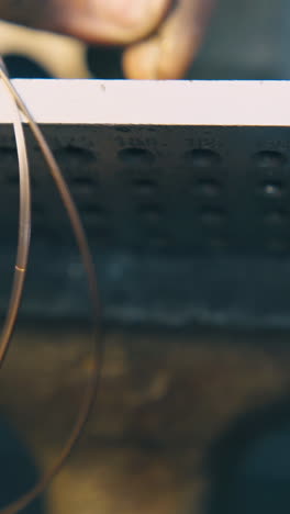 cu shot: skilled jeweler pulls gold cable through hole in tool with pliers at workplace in light workshop close upper view