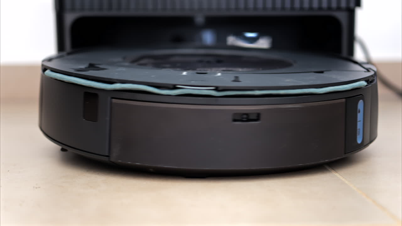 Close up of a black robot vacuum cleaner moving and rotating on the floor tiles