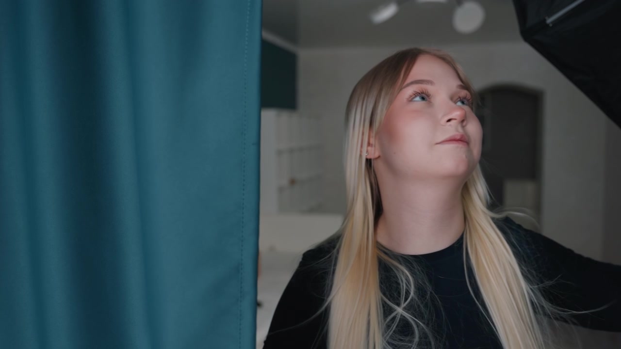 Donna bionda chiara sistema tende color verde acqua con mani concentrate nel nuovo appartamento, misurando il posizionamento, testando luce e privacy, allestendo lo spazio abitativo, in un'azione metodica di allestimento e decorazione fai-da-te.