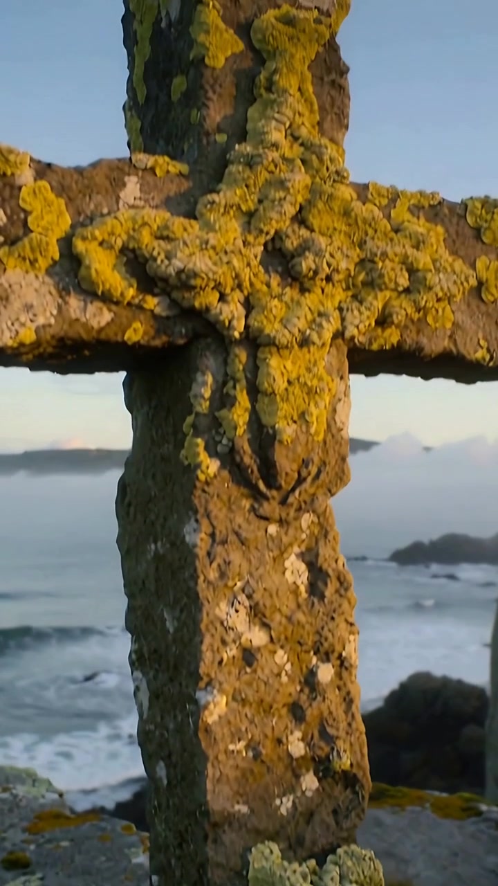 Video verticale: Telecamera che si inclina rivelando una croce di pietra su una riva rocciosa, documentando la texture del lichene
