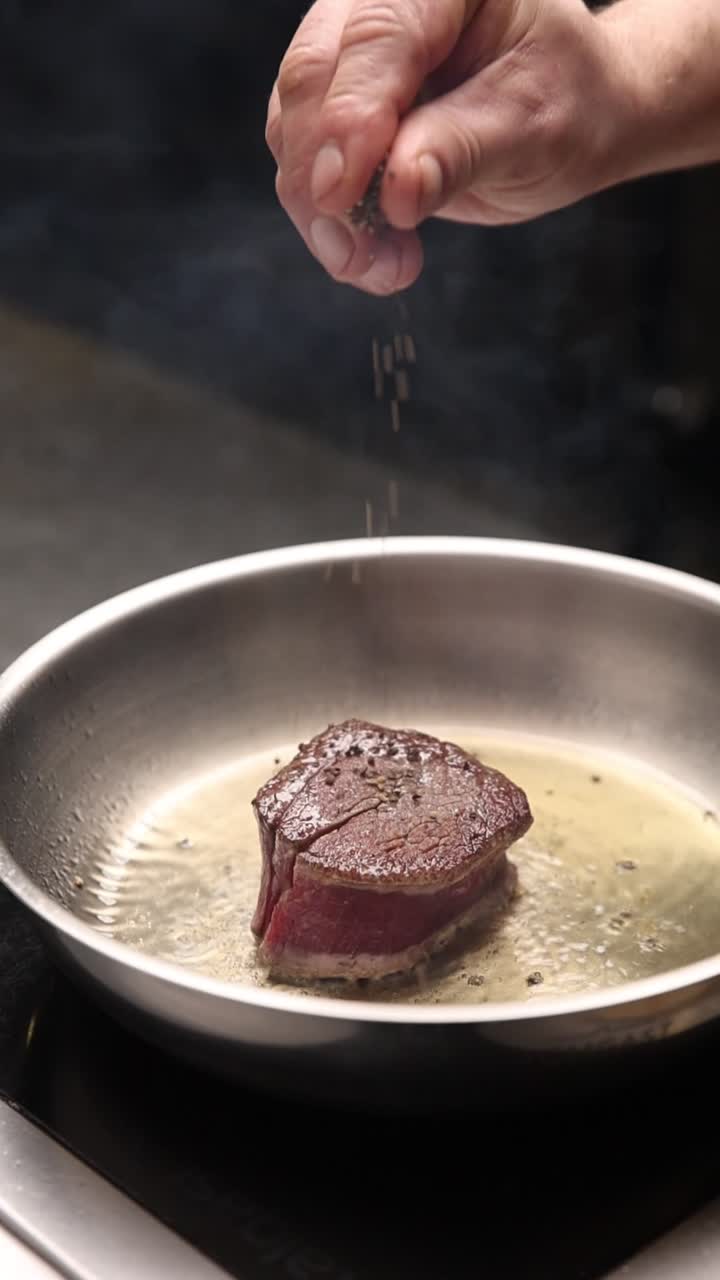 Chef professionista che condisce un filetto in una padella calda