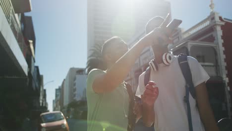 two happy mixed race male friends standing, talking and using smartphone in the street