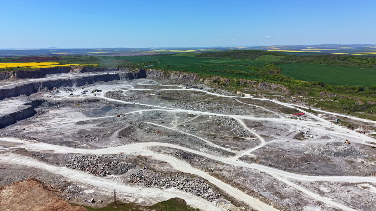 Attività di costruzione e minerarie in una grande cava sotto un cielo azzurro brillante e un paesaggio verde.