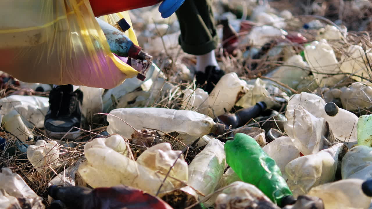 Man collecting scattered plastic bottles from the ground in the nature