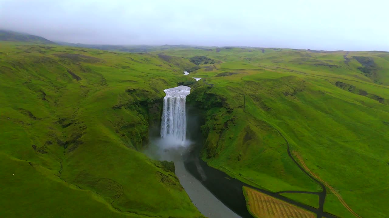 Experience the breathtaking beauty of Skógafoss waterfall from a drone’s perspective, showcasing its majestic cascade surrounded by lush greenery in Iceland.