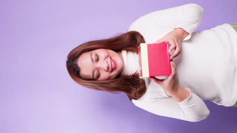 retrato vertical hermoso de una mujer feliz asiática sosteniendo una caja de regalo roja aislada sobre un fondo violeta-3