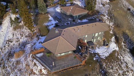 a large house is seen atop a bluff with snowy grass and trees beside it