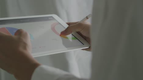 un hombre de negocios asiático de primer plano scrolling tablet examinando informes financieros y analizando el crecimiento del negocio en la oficina.