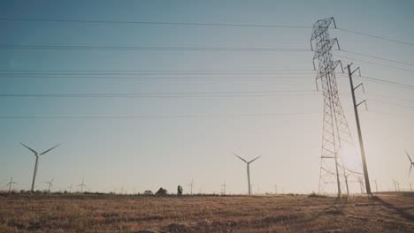 Ein-Windmühlenpark-Und-Strommasten-Auf-Einem-Feld