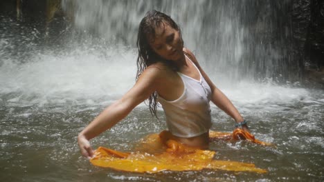 a young woman with long, dark hair is dancing in the water with a yellow piece of fabric in slow motion