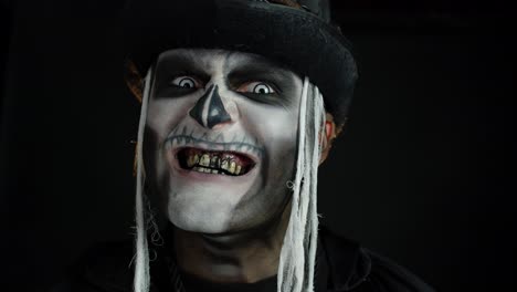 Sinister-man-with-skull-makeup-appearing-on-black-background,-making-faces-and-ominous-smile