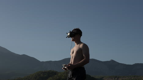 young man with goggles and remote controlling fpv drone flying by in outdoors