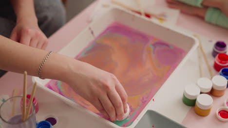 young woman puts egg into tray with mix for marbling design