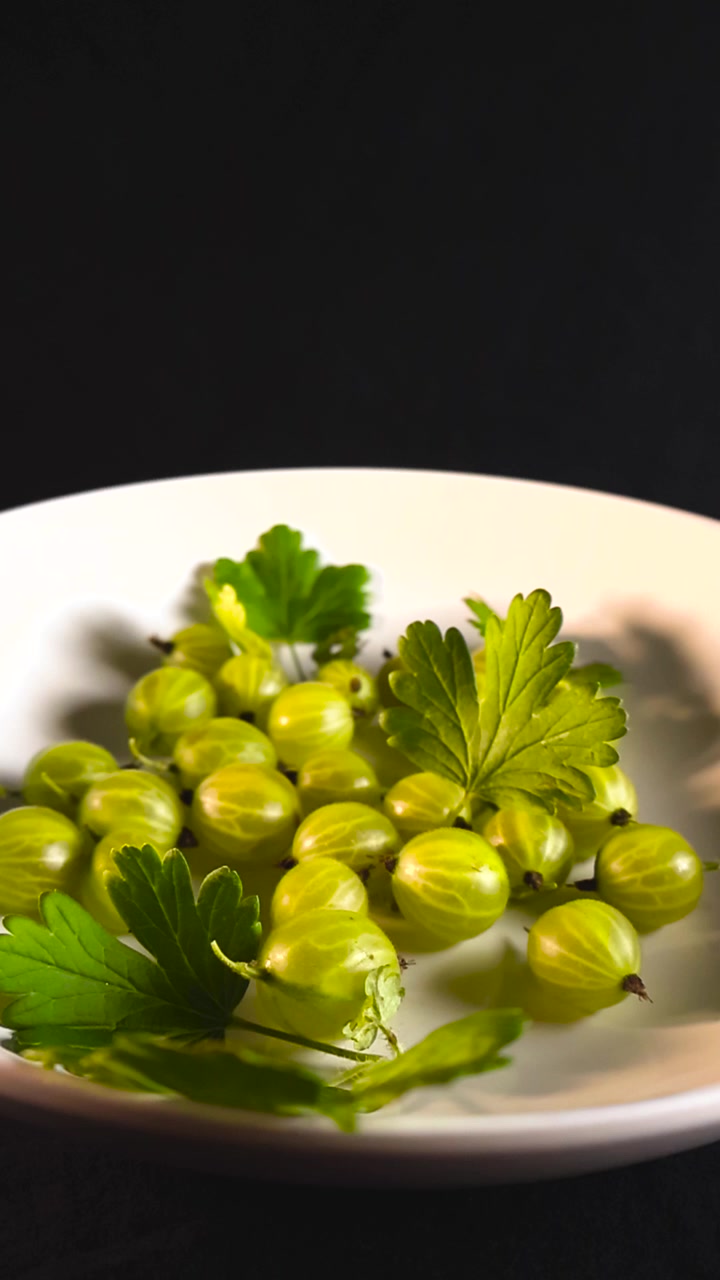 Deliziose uva spina biologiche con foglie verdi fresche adagiate in un piatto di ceramica bianco su uno sfondo scuro, che rappresentano un'alimentazione sana, cibo ricco di vitamine e il raccolto estivo.