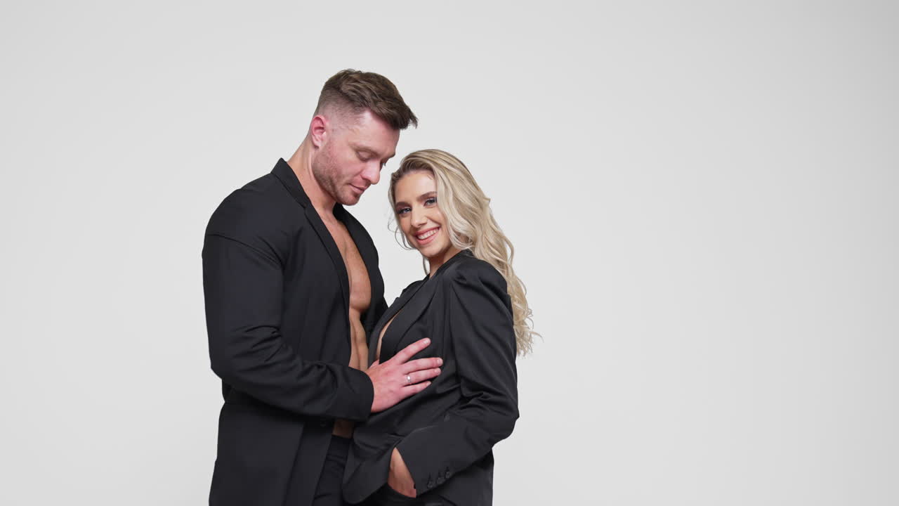 Beautiful couple in love wearing black suits. Studio footage of man and woman embracing. White backdrop.