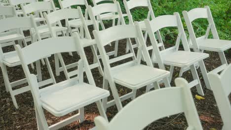 a slow pan of empty white wooden chairs set up in a forest wedding venue